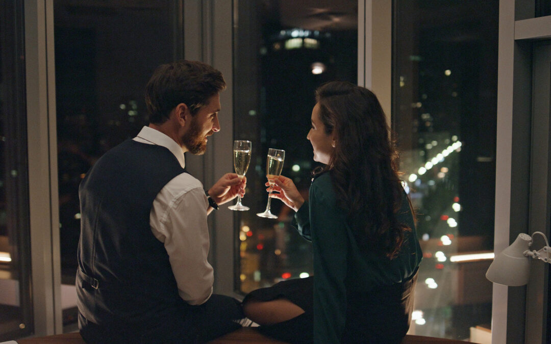 Lovely couple enjoying champagne on romantic evening date sitting at window.